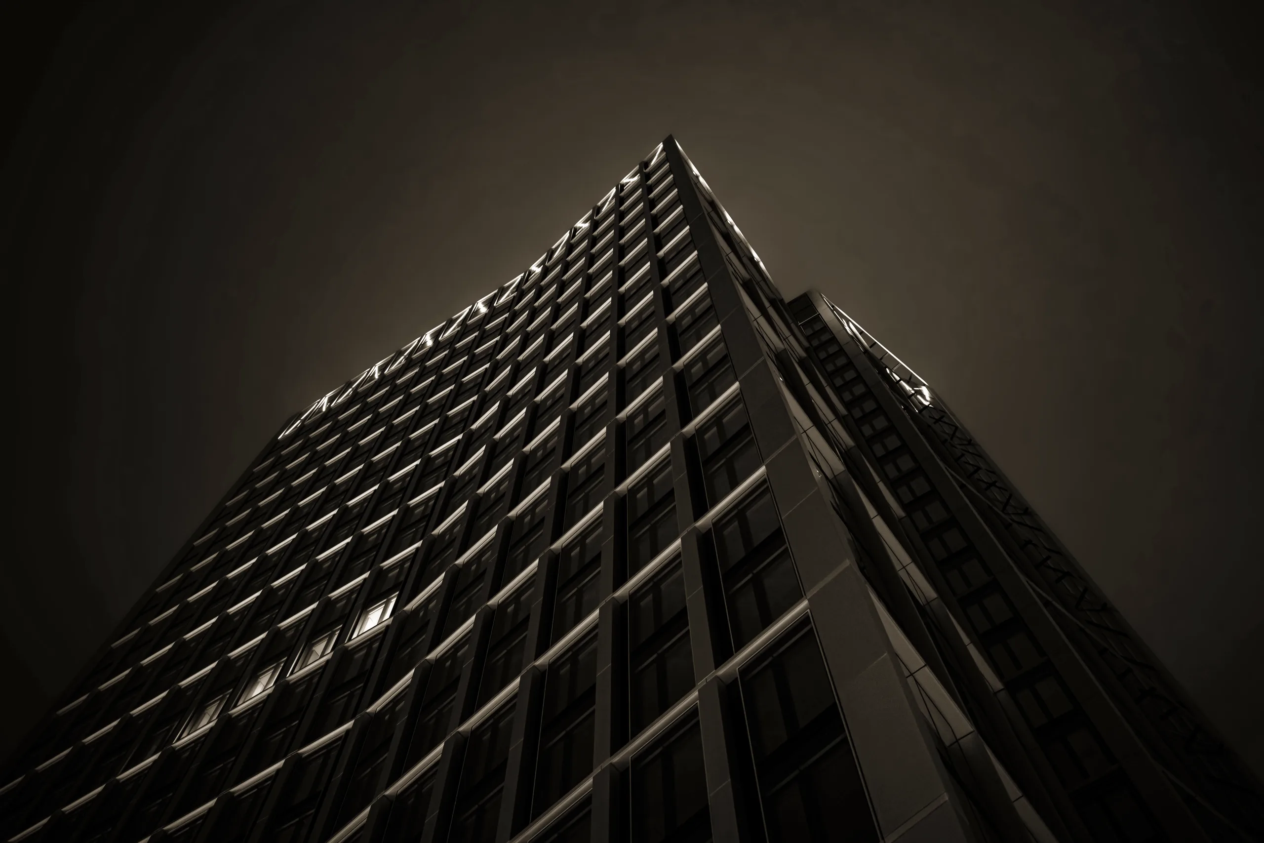 Low-angle view of a dark tower, its facade receding into repeating bands of glass and shadow